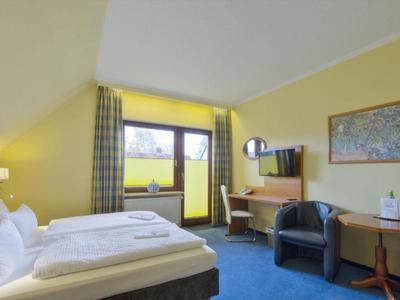 Helles Hotelzimmer mit Doppelbett, blauem Teppich und Blick auf eine grüne Landschaft.