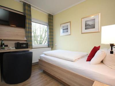 Kleines Hotelzimmer mit Einzelbett, Fernseher und Fensterausblick.