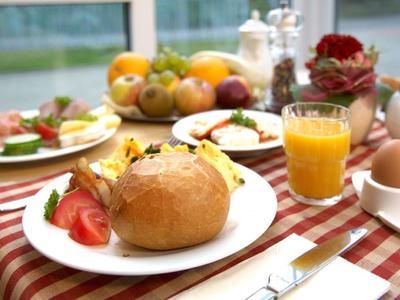 Breakfast table with bread roll, orange juice, egg, and fresh fruit on a checkered cloth.