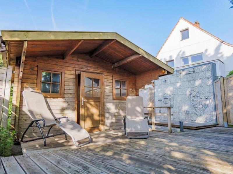 Cozy wooden patio with lounge chairs in front of a small garden house in bright sunlight.
