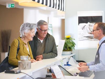 Älteres Paar spricht freundlich mit einem Hotelrezeptionisten am Empfangstresen.