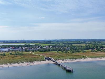Beach with long pier and green landscape in the background under cloudy sky