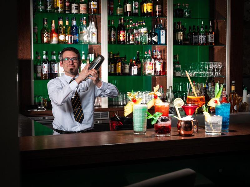 Bartender shakes colorful cocktails behind the hotel bar counter.