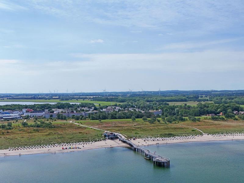Beach with long pier and green landscape in the background under cloudy sky