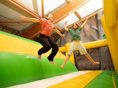 Zwei Kinder springen fröhlich auf einer bunten Hüpfburg in einem Innenraum.