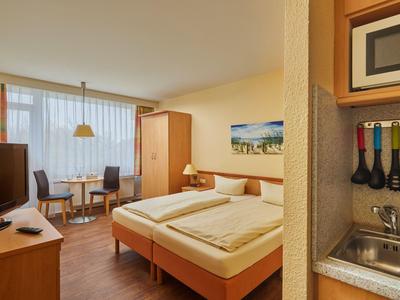 Gemütliches Hotelzimmer mit Doppelbett, Esstisch und Küchenzeile mit Mikrowelle.