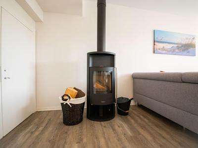 Moderner Holzofen in einem hellen Wohnzimmer mit grauem Sofa und Holzkorb.