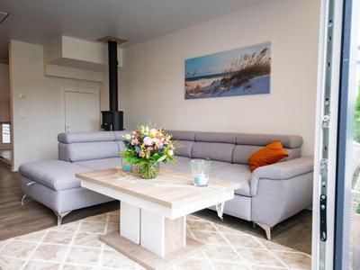 Helles Wohnzimmer mit grauem Ecksofa, Holztisch und Blumenstrauß auf dem Tisch.