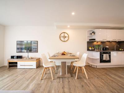 Moderner Wohn- und Essbereich mit Holzboden, weißem Esstisch und Küchenzeile in hellem Raum.