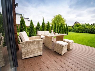 Gemütliche Gartenmöbel aus Rattan auf einer Terrasse mit Blick auf einen gepflegten Garten.