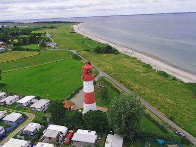 Roter und weißer Leuchtturm nahe Strand und Campingplatz an der Küste.