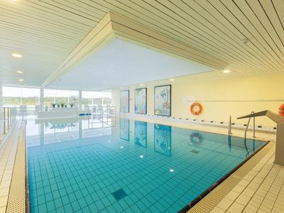 Ogrzewany basen kryty z niebieskimi płytkami, dużymi oknami i białymi ścianami.