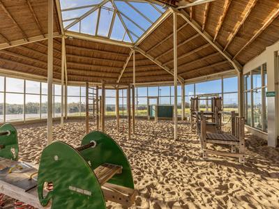 Zadaszony plac zabaw dla dzieci z piaskową nawierzchnią i sprzętem pod drewnianą kopułą.