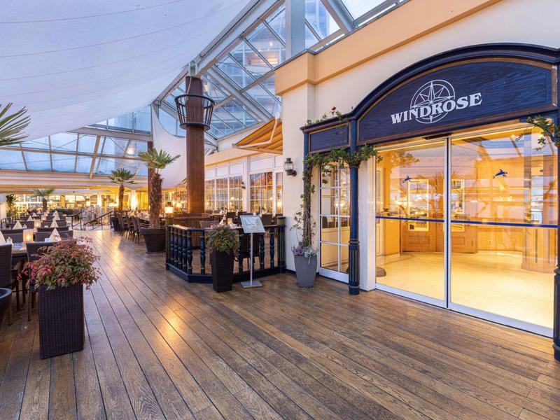 Zadaszony drewniany taras z zewnętrzną gastronomią i wejściem do sklepu o nazwie Windrose.