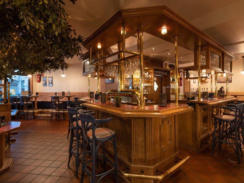 Przytulny bar hotelowy z drewnianym kontuarem, stołkami i ciepłym oświetleniem.