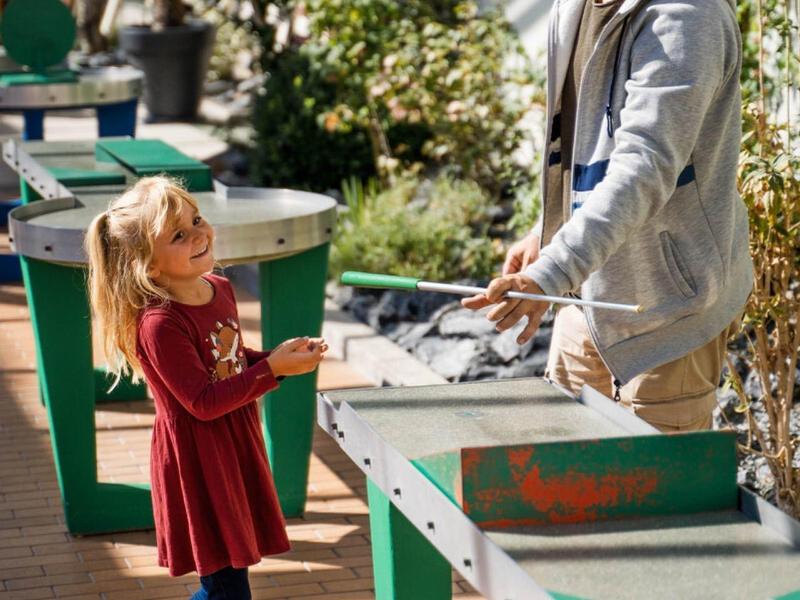 Mężczyzna i dziewczynka grają razem przy stole do piłkarzyków na zewnątrz w świetle dziennym.