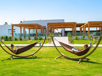 Zwei Personen entspannen in Hängematten auf grünem Rasen vor modernen Pavillons bei klarem Himmel.