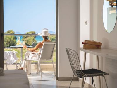 Blick von einem Hotelzimmer auf eine Terrasse mit Person und Meer im Hintergrund.
