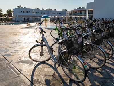 Reihe von Fahrrädern mit Körben vor einem Hotel im Sonnenlicht.