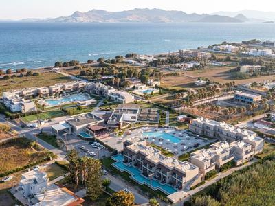 Luftaufnahme eines Resorts mit Pools, umgeben von Meer, Stränden und Bergen im Hintergrund.