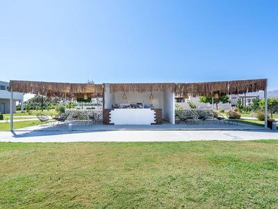 Moderner, offener Pavillon mit Holzdach, umgeben von gepflegtem Rasen und klarem blauen Himmel.