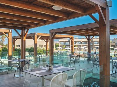 Überdachter Außenbereich mit Tischen und Stühlen auf einer Terrasse neben einem Hotel.