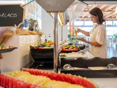 Frau wählt frische Salate an einem Buffet in einem hellen, modernen Speisesaal.