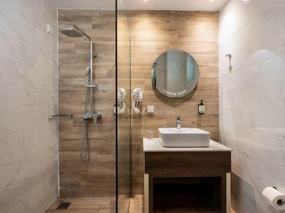 Moderne Badezimmer mit Holzvertäfelung, runder Spiegel, Waschbecken und Glasdusche im Hotelzimmer.
