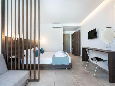 Modernes Hotelzimmer mit Doppelbett, Schreibtisch, TV und einem grauen Sofa.