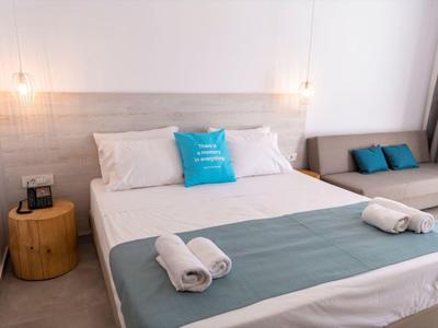 Modernes Schlafzimmer mit Doppelbett, weiß-blauer Bettwäsche, Holz-Nachttisch und grauem Sofa.