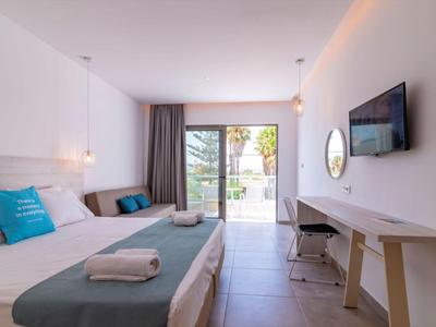 Helles Hotelzimmer mit Doppelbett, Schreibtisch, Fernseher und Terrasse mit Blick ins Grüne.