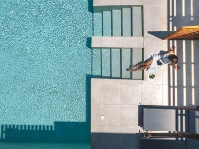 Vogelperspektive eines Pools mit Sonnenschirm, Liegestühlen und einer Person, die drinnen sitzt.