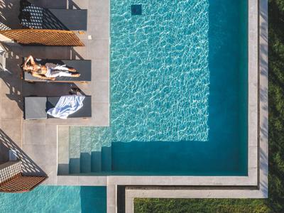 Vogelperspektive eines modernen Pools mit zwei Liegen und Sonnenschirmen neben grüner Wiese.