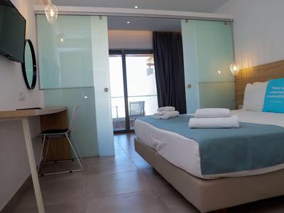 Modernes Hotelzimmer mit Doppelbett, Tisch, Stuhl, Fernseher und Balkon mit Glasschiebetür.