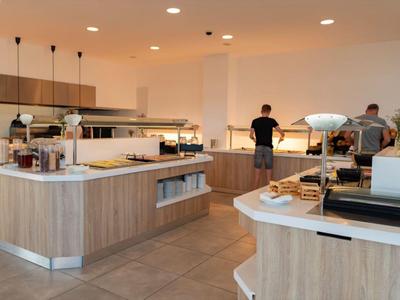 Moderne Cafeteria mit hellem Holz, Essensbuffet, Pendelleuchten und Personen am Selbstbedienungstresen.