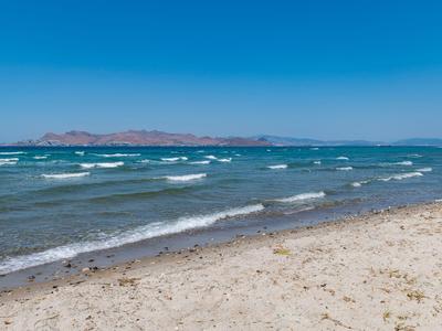 Ein Sandstrand mit leichtem Wellengang und blauer Himmel am Meer.