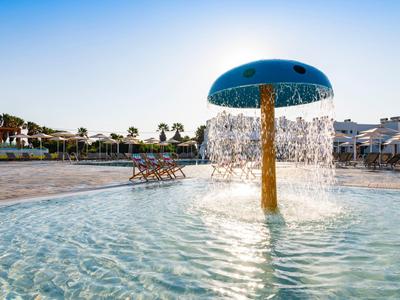 Mushroom-shaped water feature in the shallow pool area of a holiday resort on a sunny day.