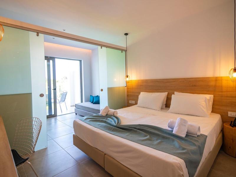 Bright hotel room with double bed, balcony, and modern lighting.