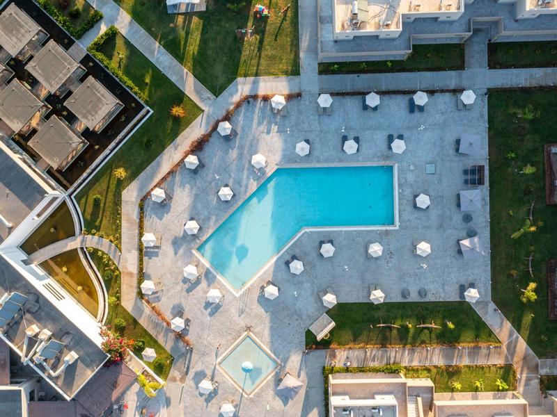 Aerial view of a hotel with a large pool and white umbrellas