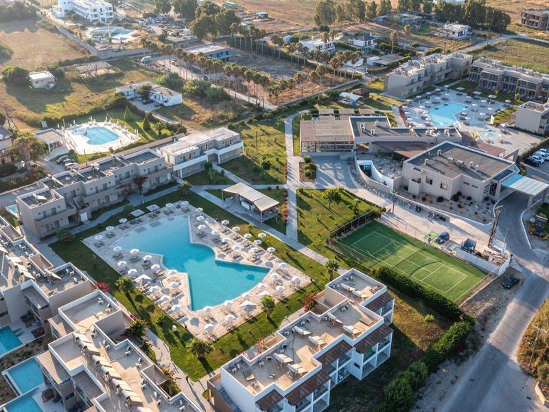 Aerial view of a hotel with multiple pools, manicured gardens, and a bright building complex.