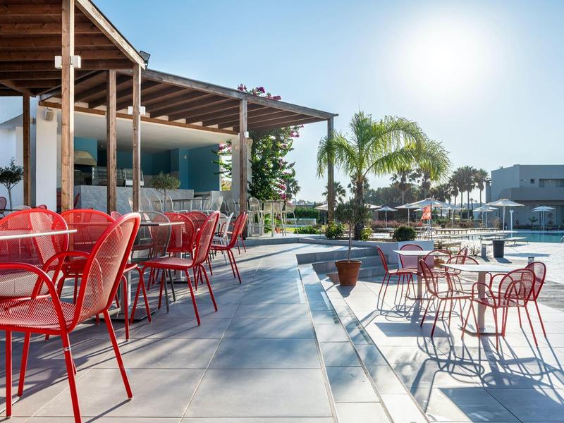 Hotel outdoor area with red chairs, pool, and palm trees on a sunny day