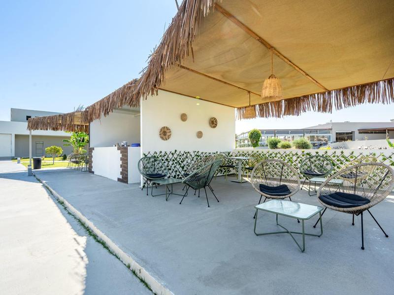 Outdoor seating area with chairs and tables under a sunshade in a modern hotel complex.