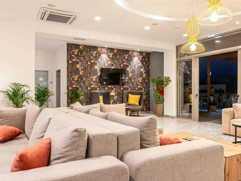 Modern hotel room with beige sofas, colorful cushions, hanging lamps, and panoramic windows at night