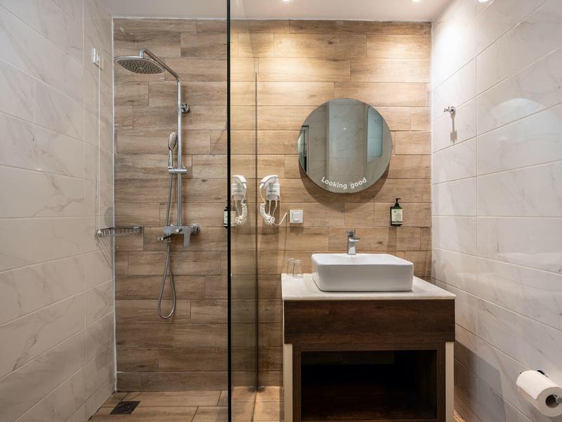 Modern hotel bathroom with wooden accents, glass shower, and round mirror