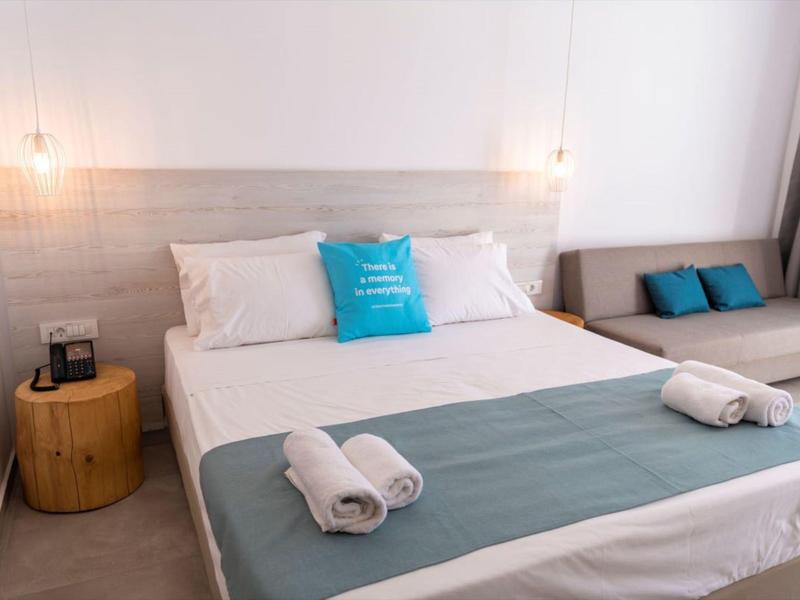 Modern hotel room with large bed, blue accents, and wooden furniture in a bright setting.