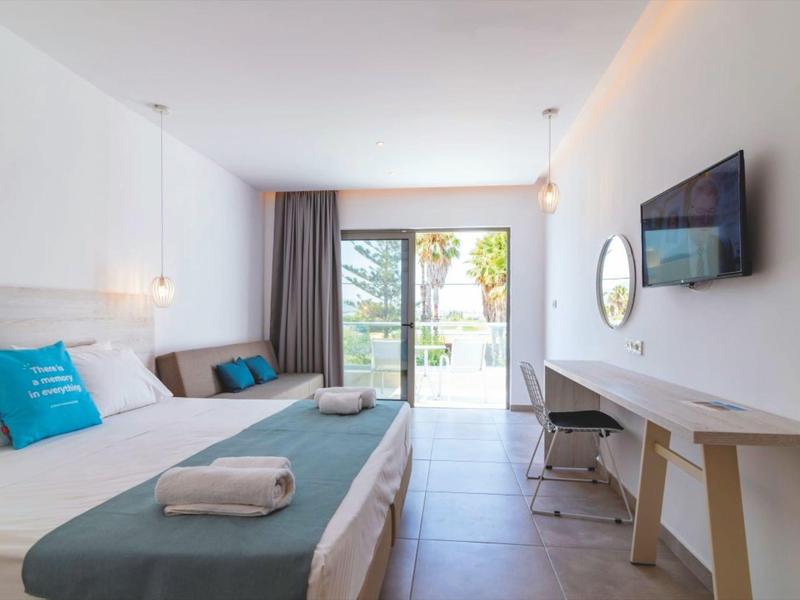 Modern hotel room with double bed, desk, chair, balcony, and flat-screen TV