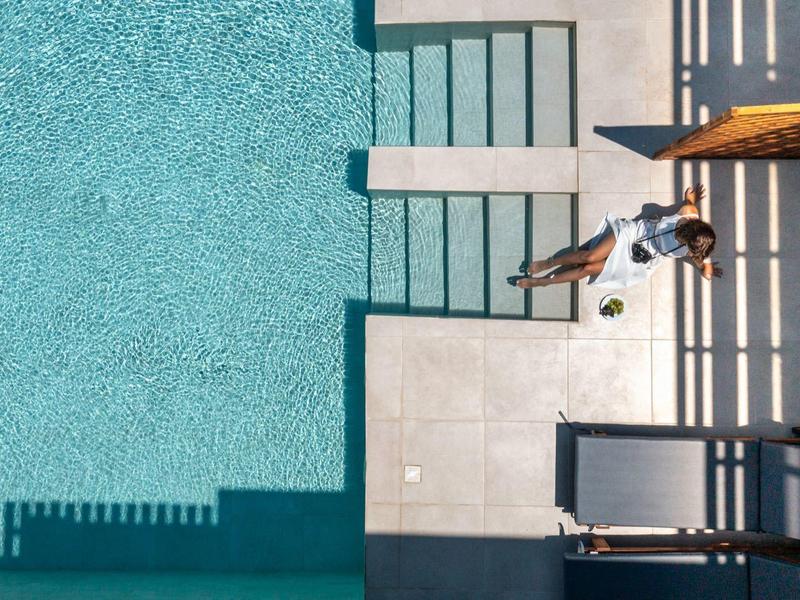 A man relaxes on a lounge chair beside a clear pool on a hotel terrace.