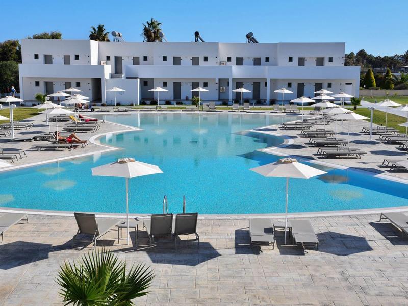 Large outdoor pool with white sun loungers and umbrellas in front of a modern hotel building.