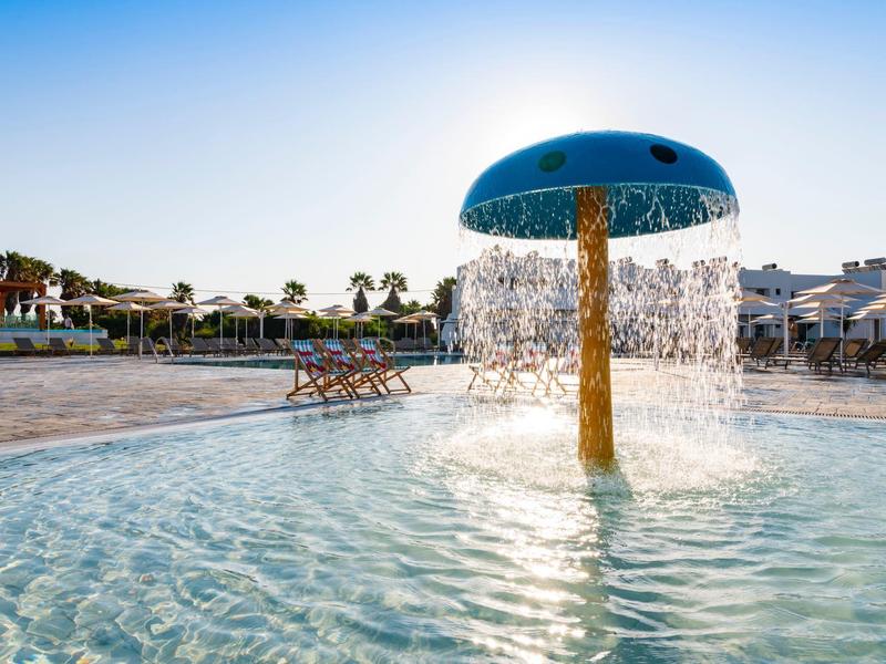 Mushroom-shaped water feature in the shallow pool area of a holiday resort on a sunny day.