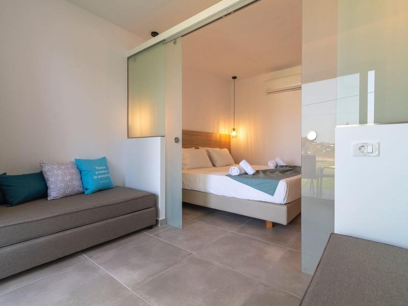Modern hotel room with double bed, sofa, and glass sliding door.